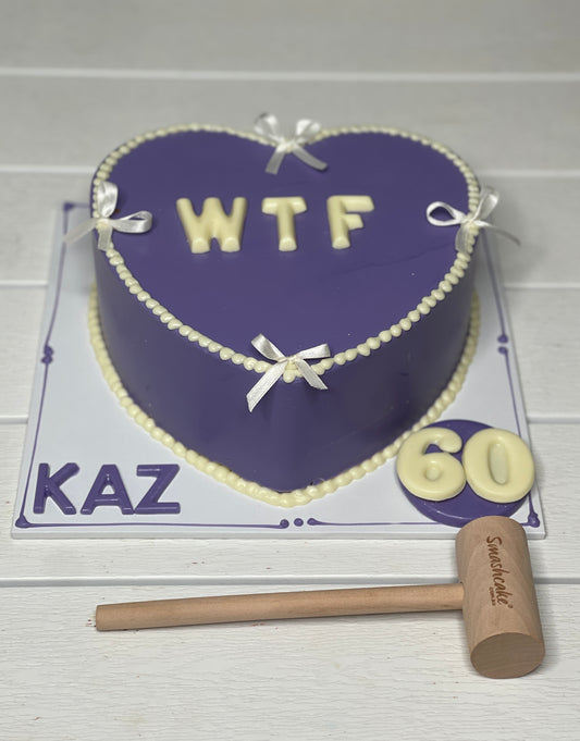 Heart-shaped cake with 'WTF' and number '60', accompanied by a mallet, on a white background.